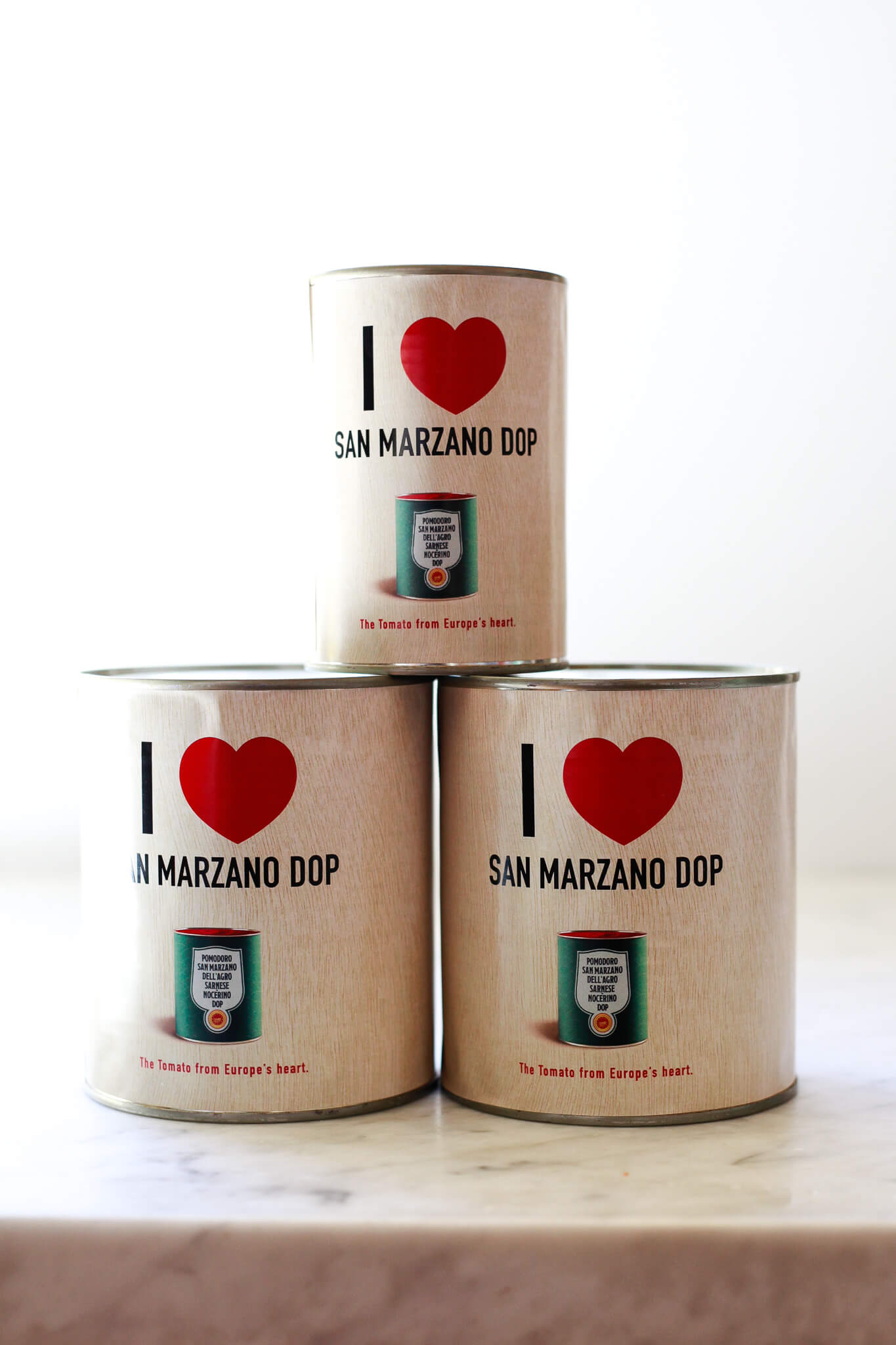 Three cans with I heart San Marzano DOP labels sit on a white marble countertop. 