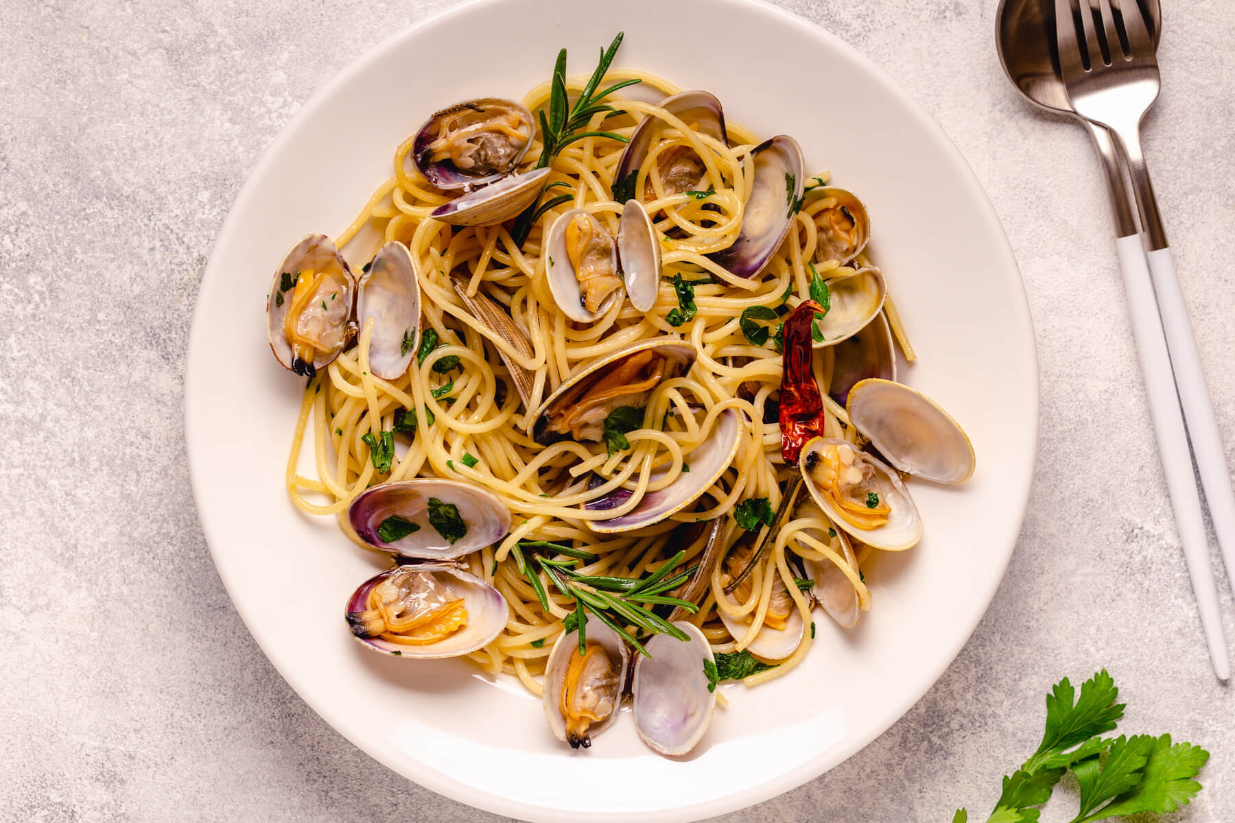 A white bowl of Italian spaghetti with clams on a concrete background. 