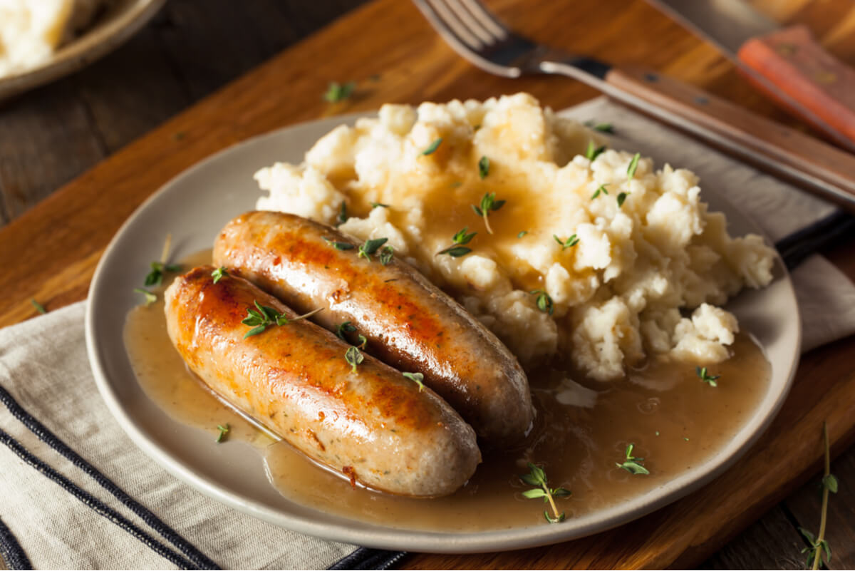 A ceramic plate topped with Bangers and Mash, a traditional British food consisting of two sausages, mashed potatoes, and gravy. 