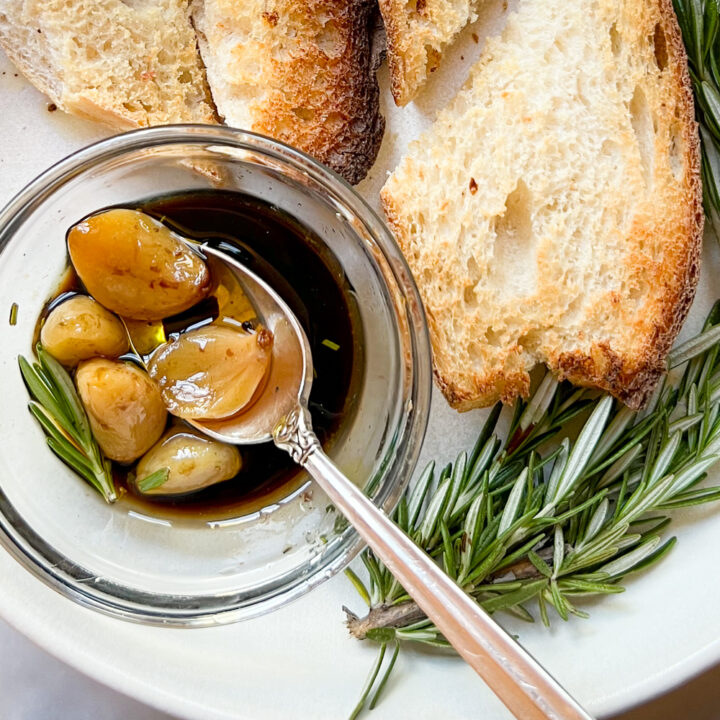 A small dish filled with homemade garlic confit and balsamic on a white plate with bread.