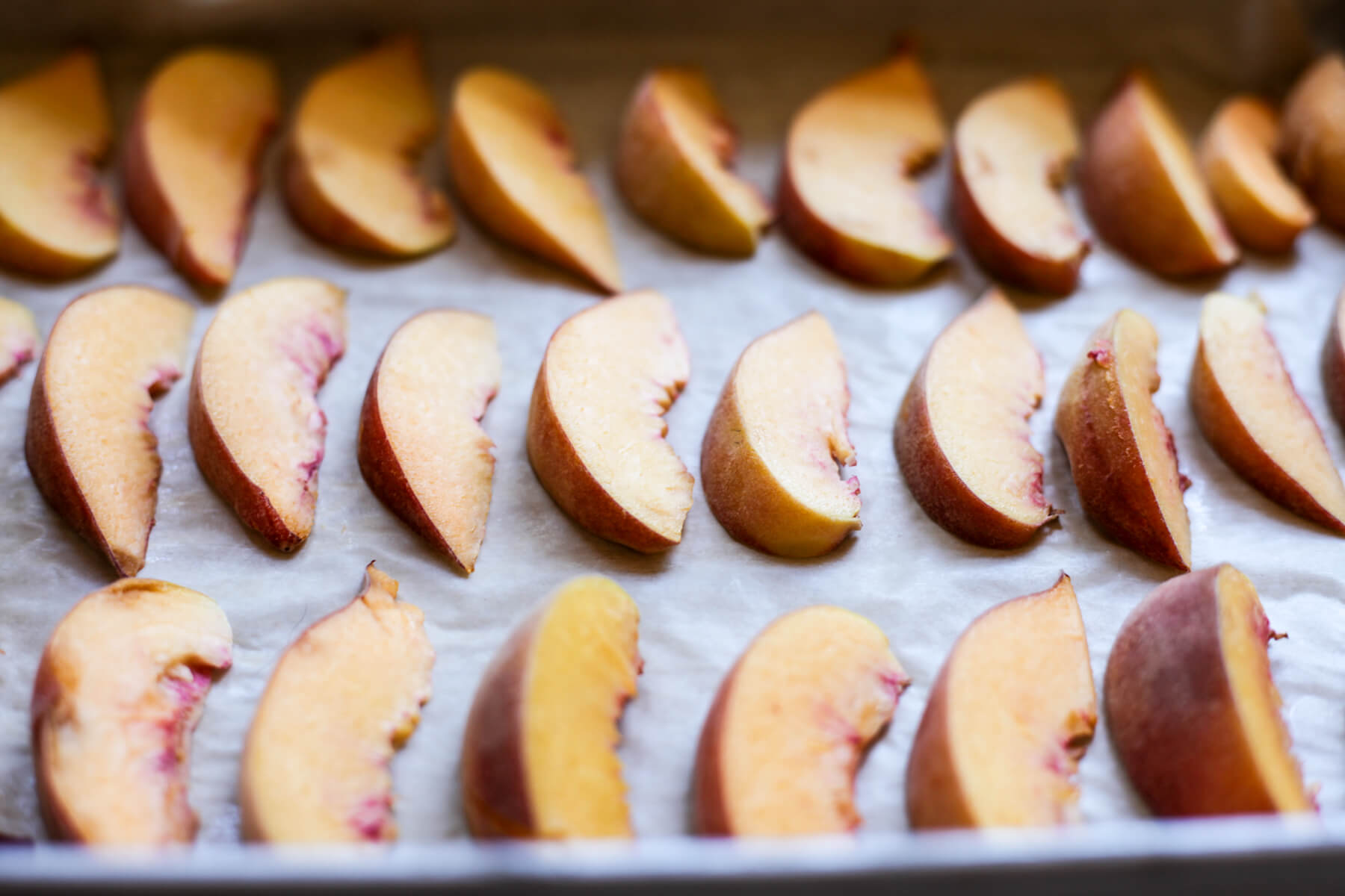 Peach slices lined up on a cookies sheet to freeze.
