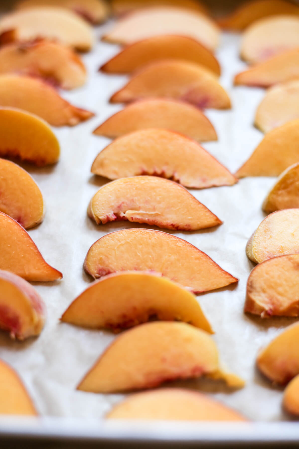 Frozen peach slices lined on a cookie sheet just out of the freezer. This shows how to freeze peaches. 