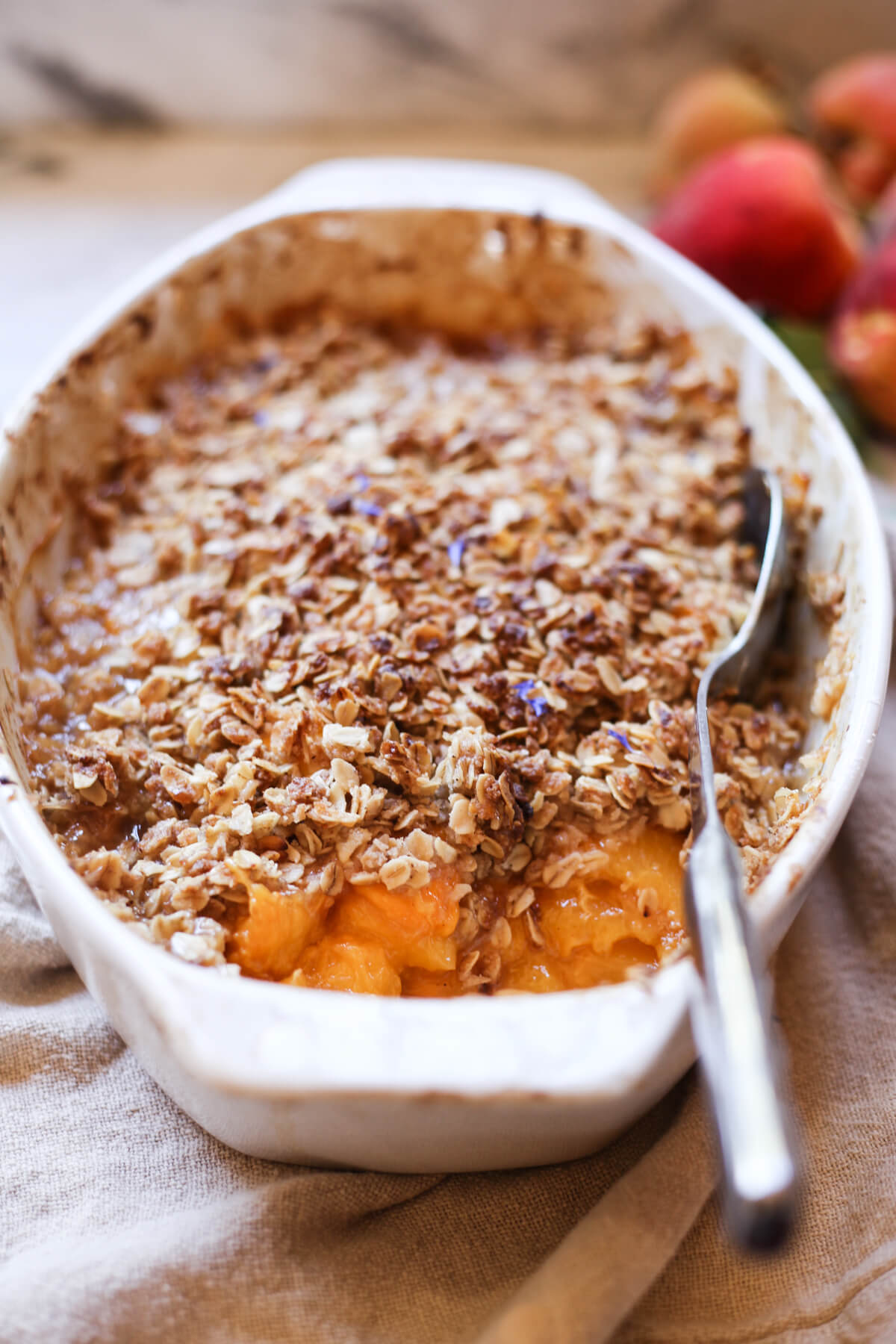 A white ceramic baking dish filled with a warm peach crisp made with fresh peaches and oat topping. 