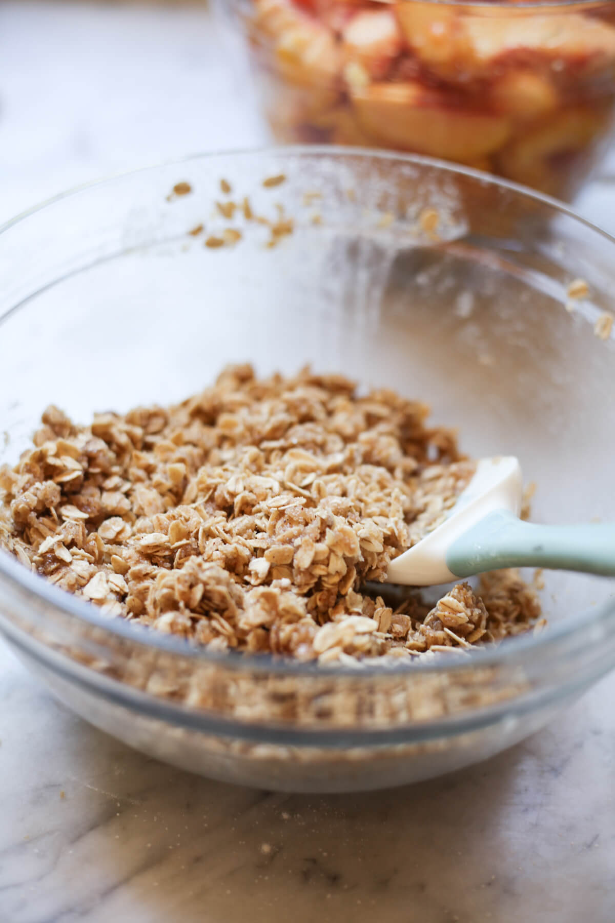 Oat crumble topping is mixed together with a rubber spatula in a glass bowl.