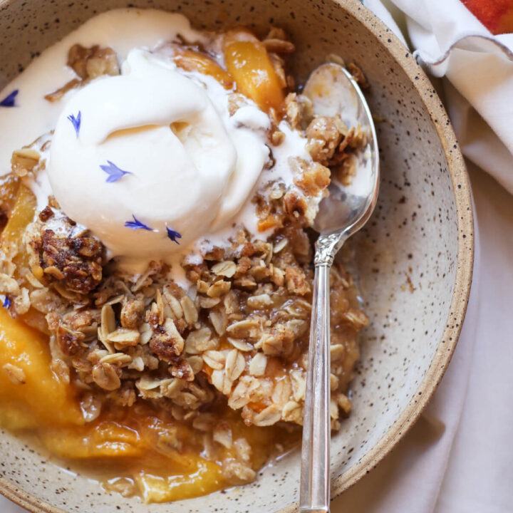An overhead photo of peach crisp with oat topping and a scoop of ice cream in an earthenware bowl.