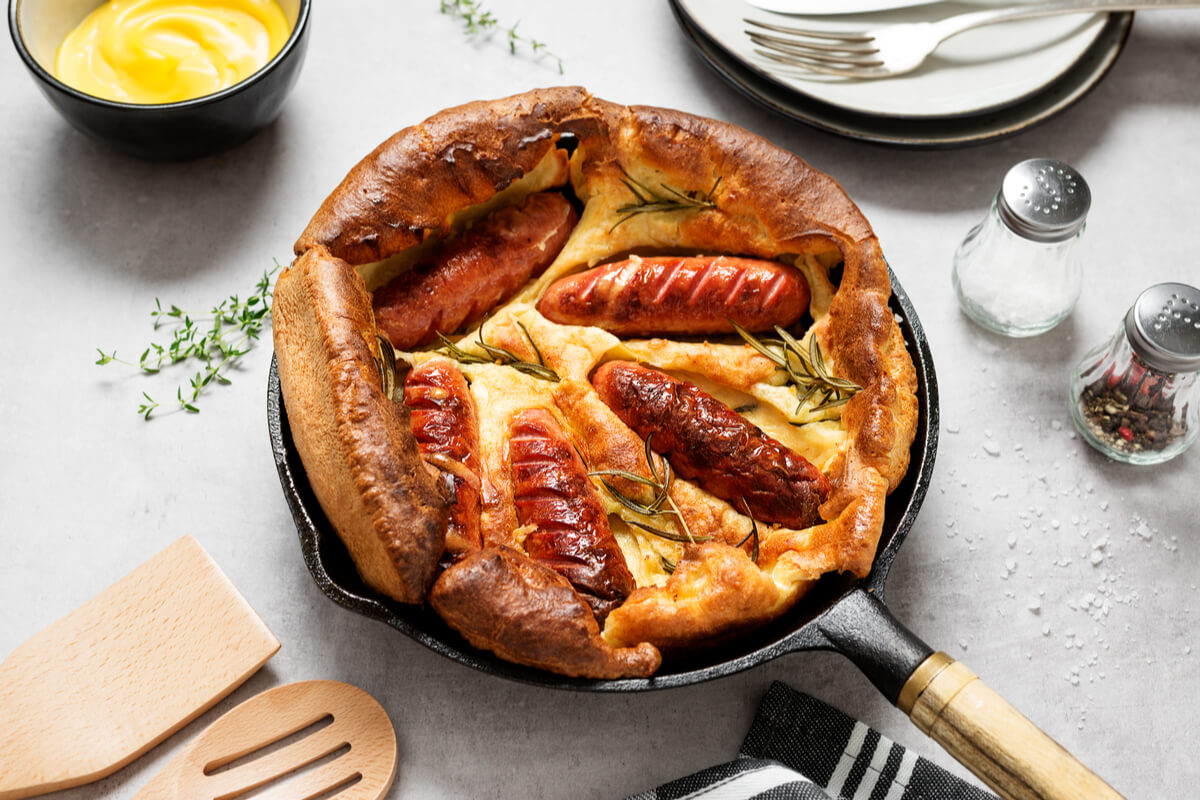 A large puffed Toad in the Hole in a black skillet. This is a traditional British food consisting of sausages baked into a puffed batter. 