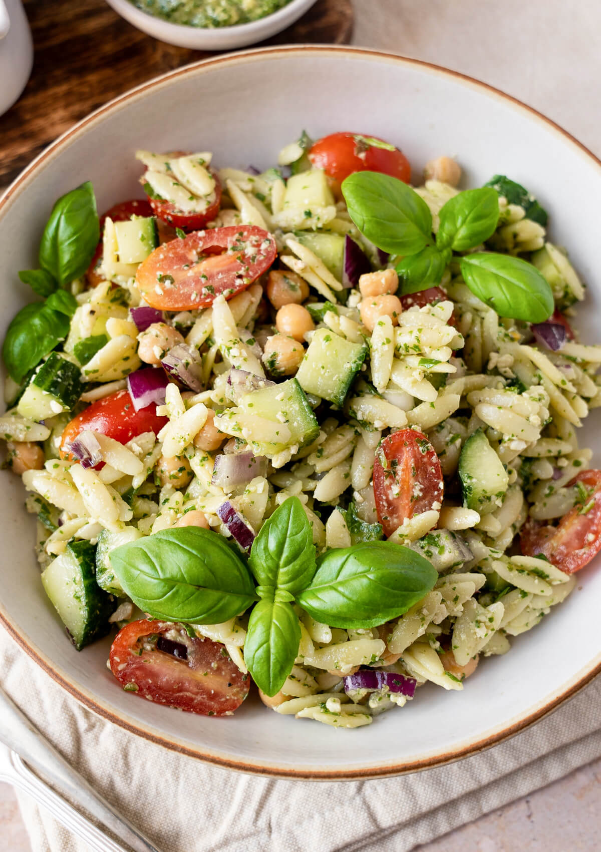 A bowl filled with a delicious pesto orzo salad with chickpeas, tomatoes, cucumbers, and basil. 
