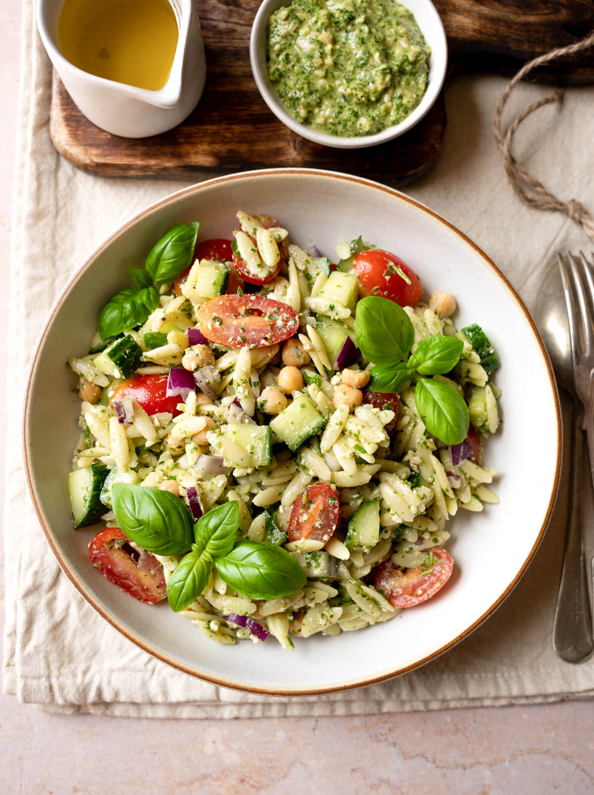 A bowl of pesto orzo salad with chickpeas, tomatoes, cucumber, and fresh basil. 