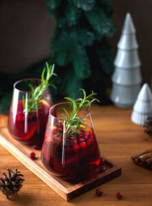 Two beautiful Christmas cocktail in stemless wine glasses. These red wine sangria drinks are garnished with rosemary sprigs.