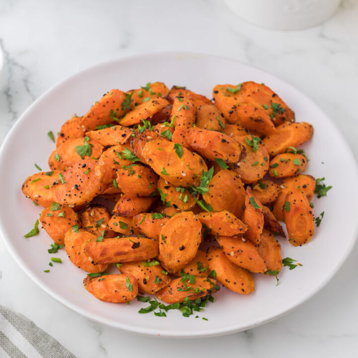 A white plate filled with air fryer sliced carrots garnished with parsley.