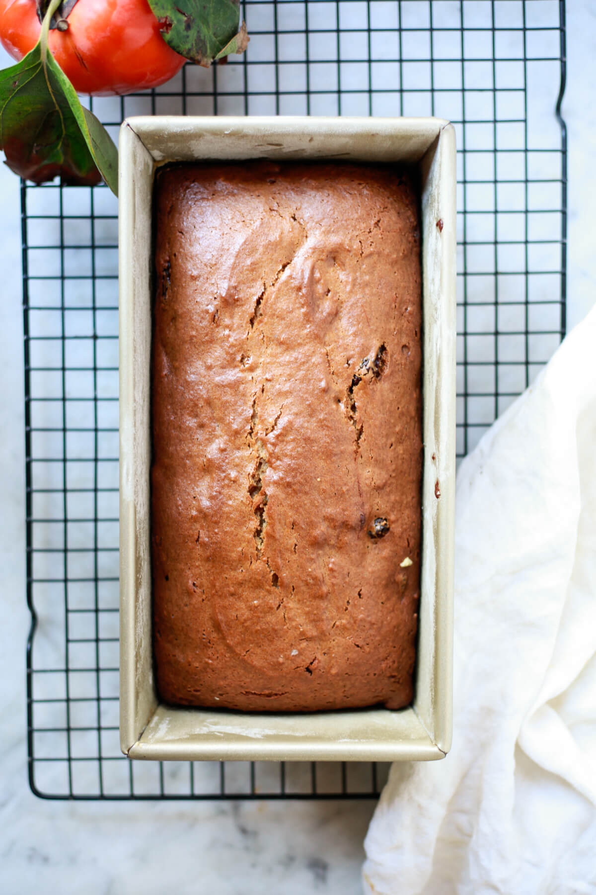 Freshly baked persimmon bread in a bold loaf pan on a cooling rack.