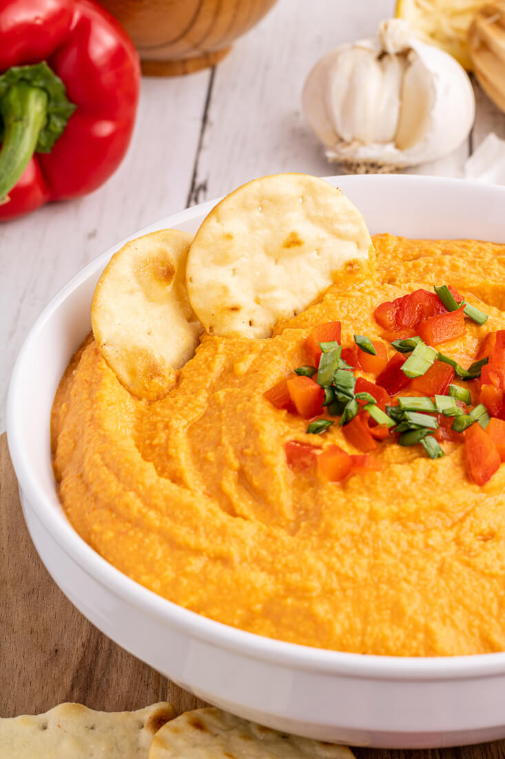 Roasted red pepper hummus in a bowl garnished with chopped roasted red pepper and chives. 