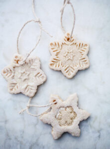 Three snowflake salt dough ornaments with twine hangers on a marble countertop.