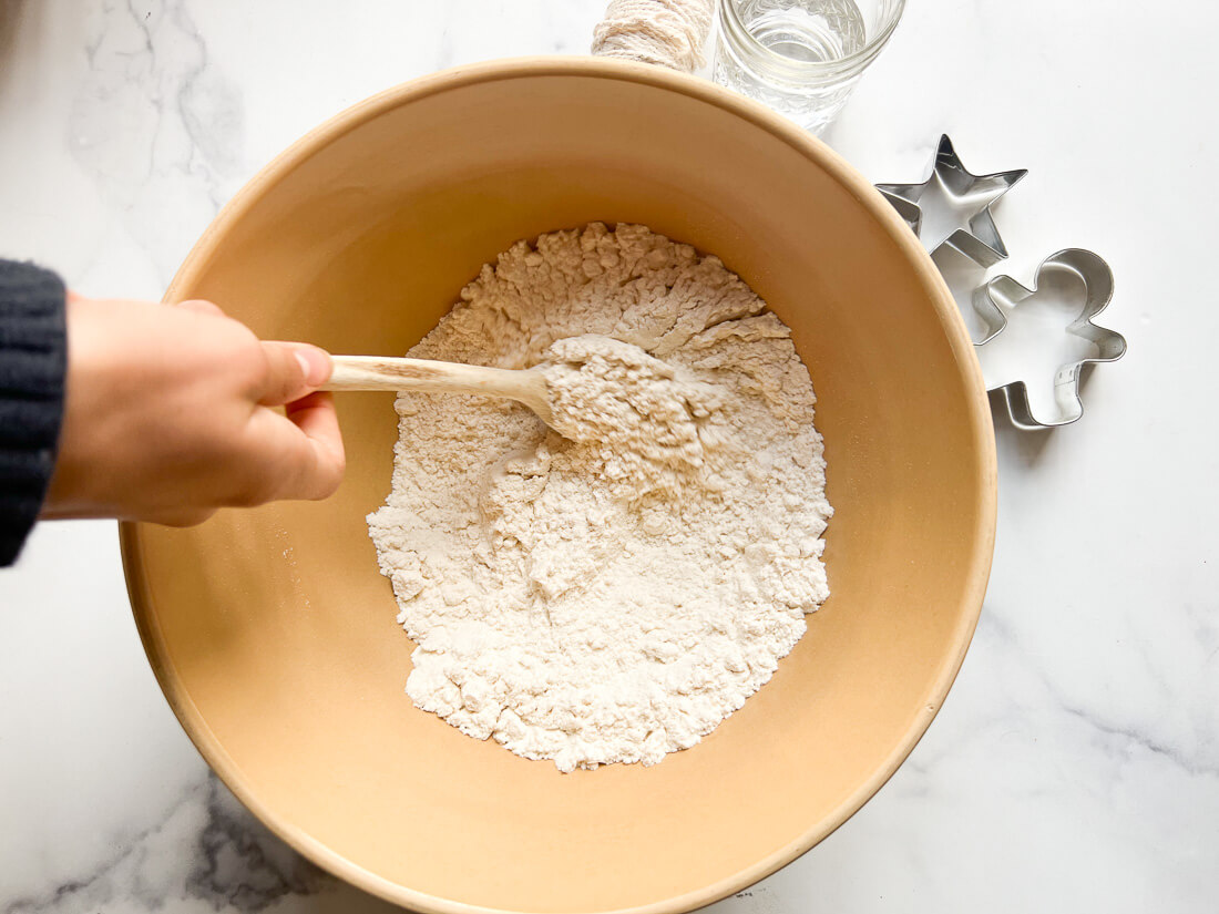 Salt and flour are mixed together in a ceramic bowl with a wooden spoon.