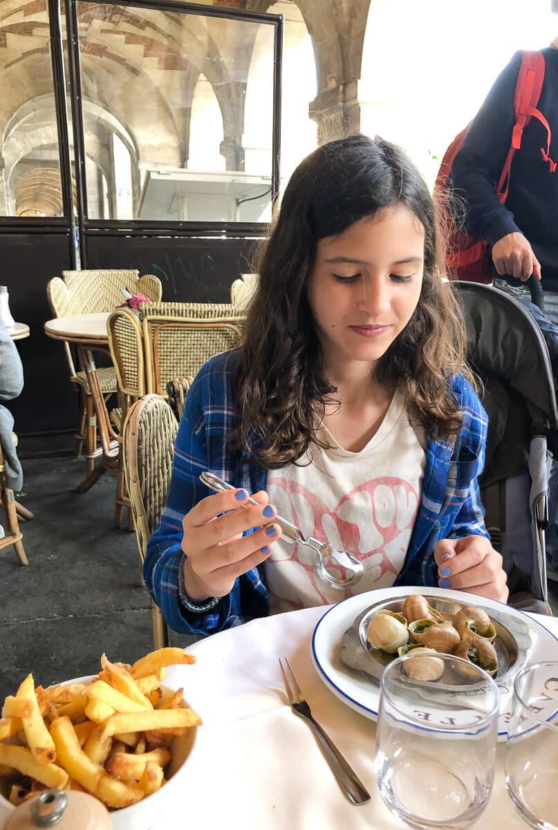 A girl eats escargot in shells with fries at Carette, and outdoor cafe in Paris. 