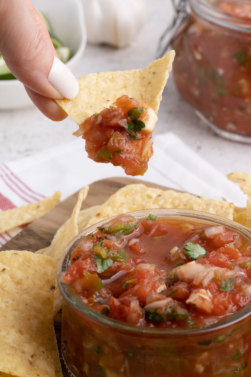 A tortilla chip is dipped into a jar of chunky homemade restaurant style salsa. 