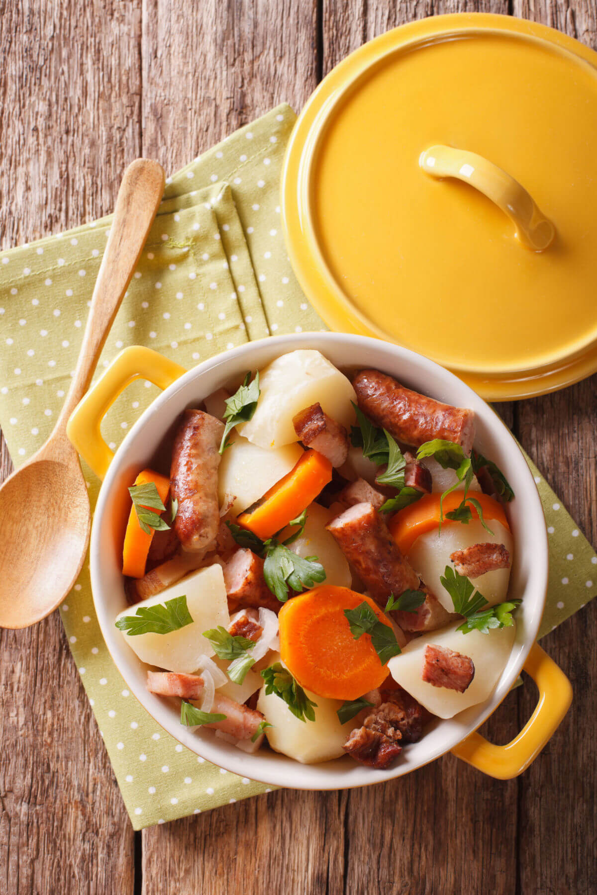 A yellow Dutch oven filled with Irish Coddle, a traditional stew made with sausages, carrots, and potatoes. 