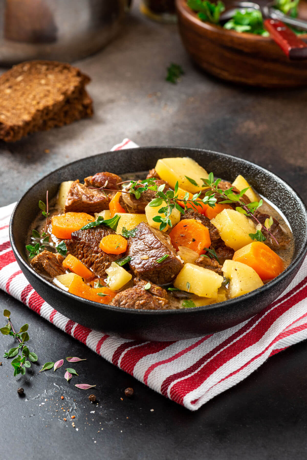 A dark ceramic dish filled with Irish stew made with beef, potatoes, and carrots and garnished with thyme. 