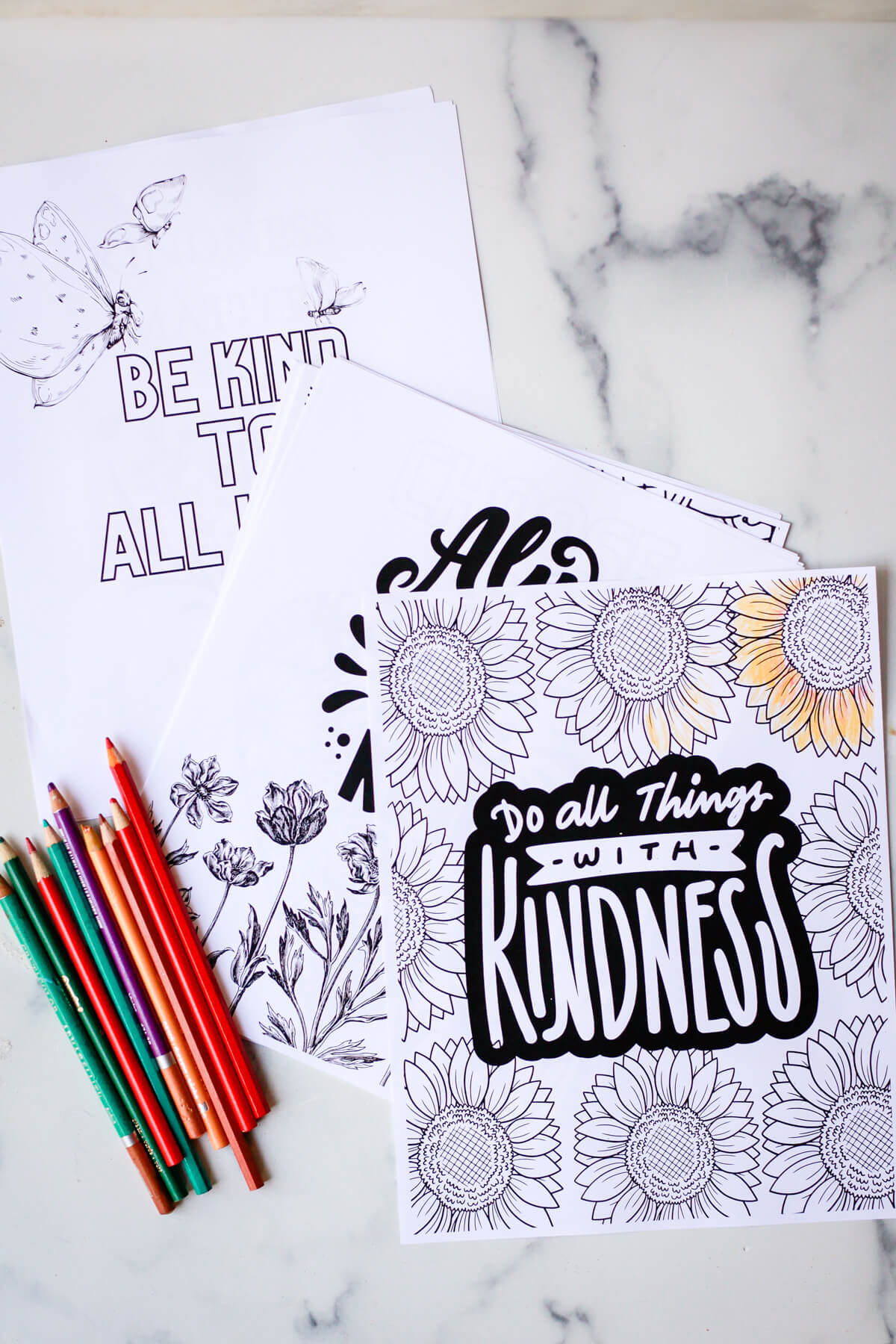 A stack of kindness coloring pages on a marble countertop with colored pencils. 