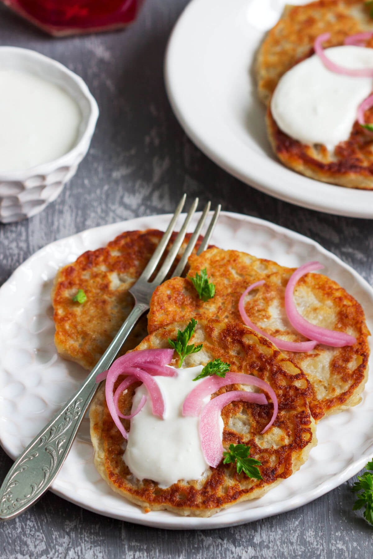 A white plate with three Irish boxty potato pancakes topped with sour cream, pickled onions, and parsley. A traditional Irish food that is vegetarian. 