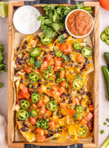 A wooden tray filled with vegetarian nachos with black beans and other toppings.