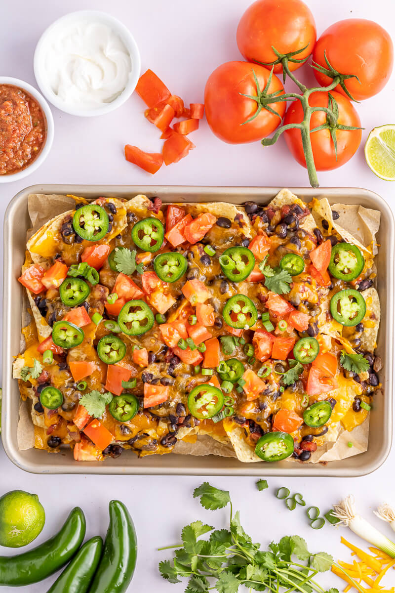 A sheet pan filled with loaded vegetarian nachos topped with jalapeno, tomato, and herbs. 