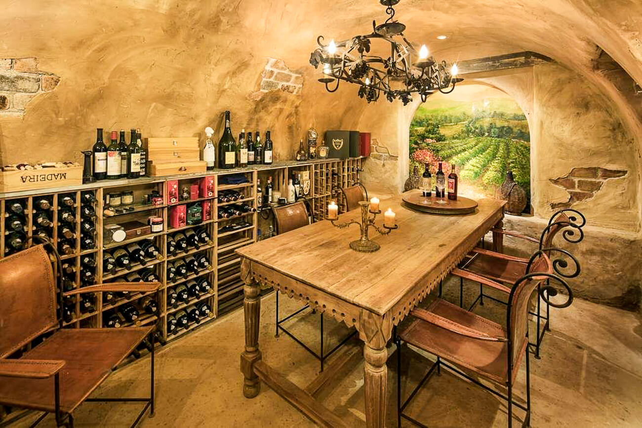 A Tuscan inspired home wine cellar tasting room with dining table and fresco on the wall. 