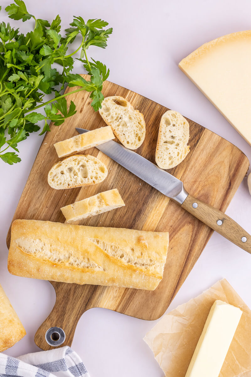 A baguette is cut into crosswise slices on a cutting board.
