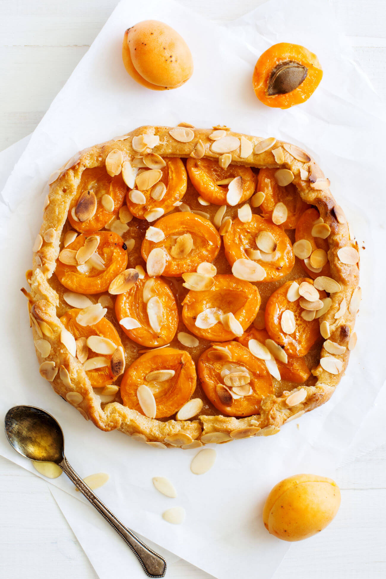 A top-down photo of a fresh apricot galette with sliced almonds on a piece of parchment paper. 