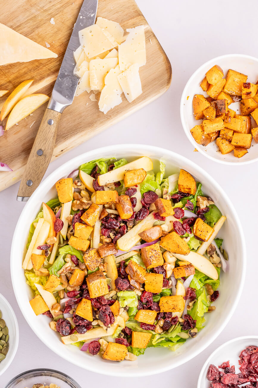 A salad bowl filled with a fall salad that includes roasted sweet potatoes, apples, cranberries and more.