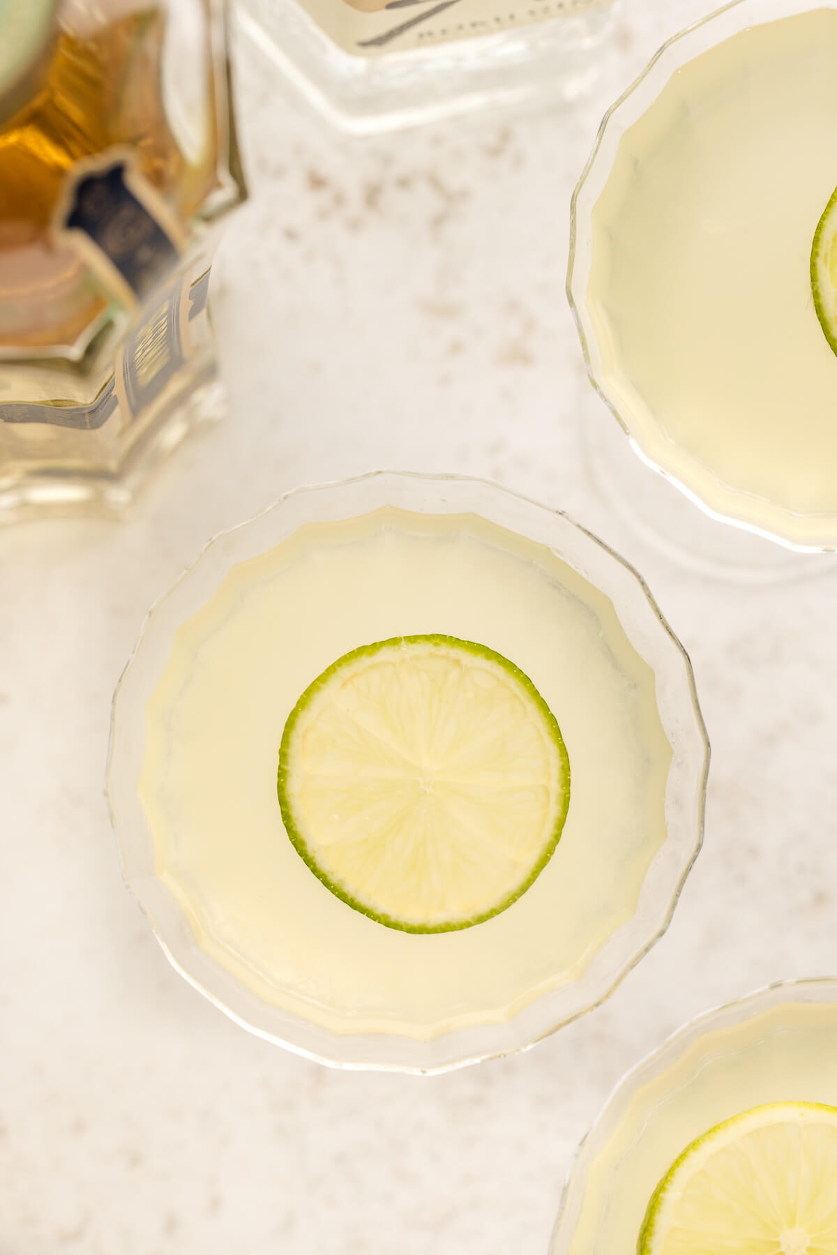 An overhead photo of three French gimlet cocktails garnished with lime. A bottle of St-Germain elderflower liqueur sits off to the side. 