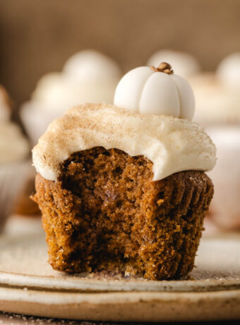 A pumpkin cupcake with cream cheese frosting with a bite out of it.