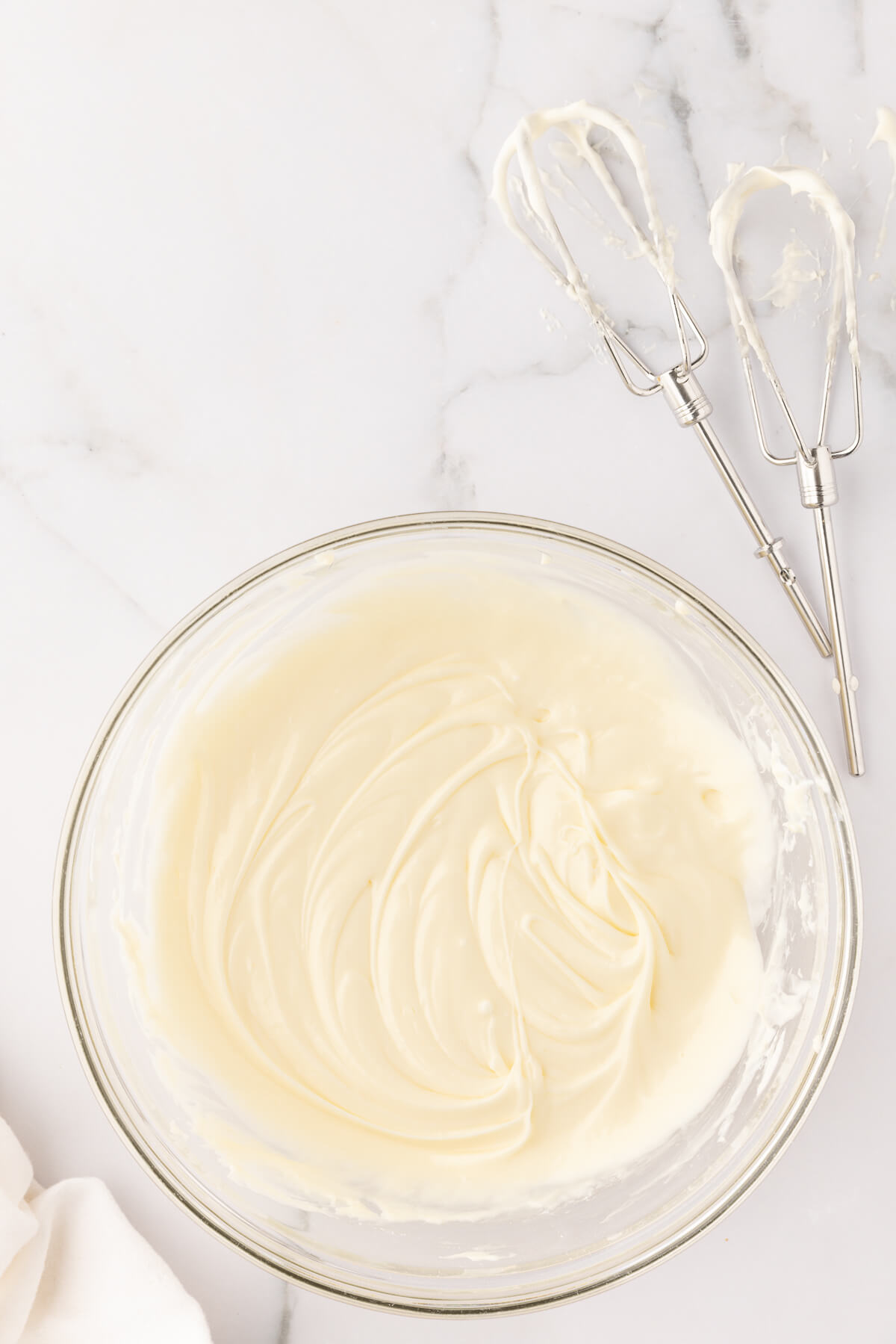 Homemade cream cheese frosting in a glass bowl on a marble countertop.