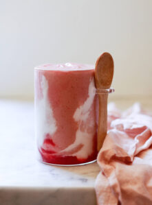 A beautiful pink smoothie with red and white swirls on a white kitchen counter.