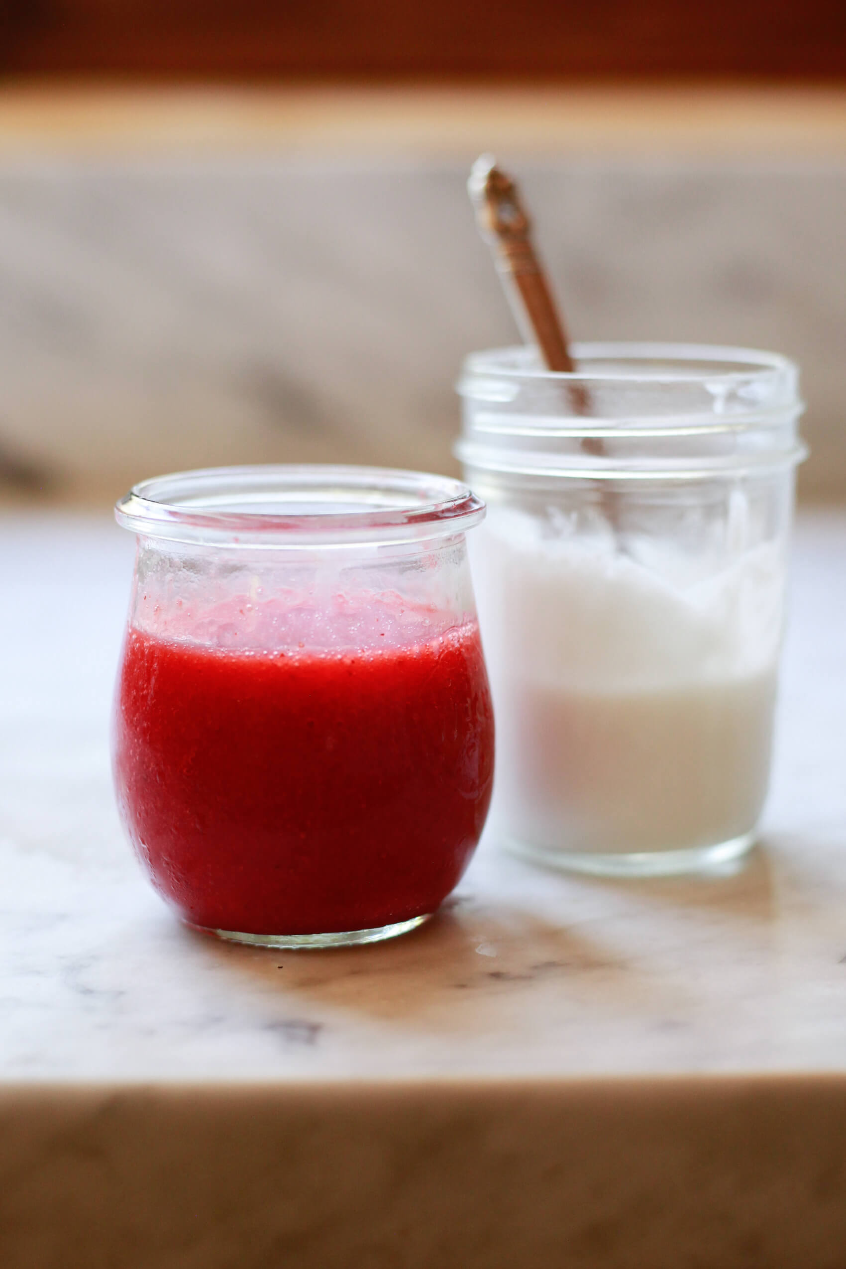 Small jars filled with Zuma Valley coconut cream homemade strawberry glaze sit on a kitchen counter before making a Hailey Bieber smoothie. 