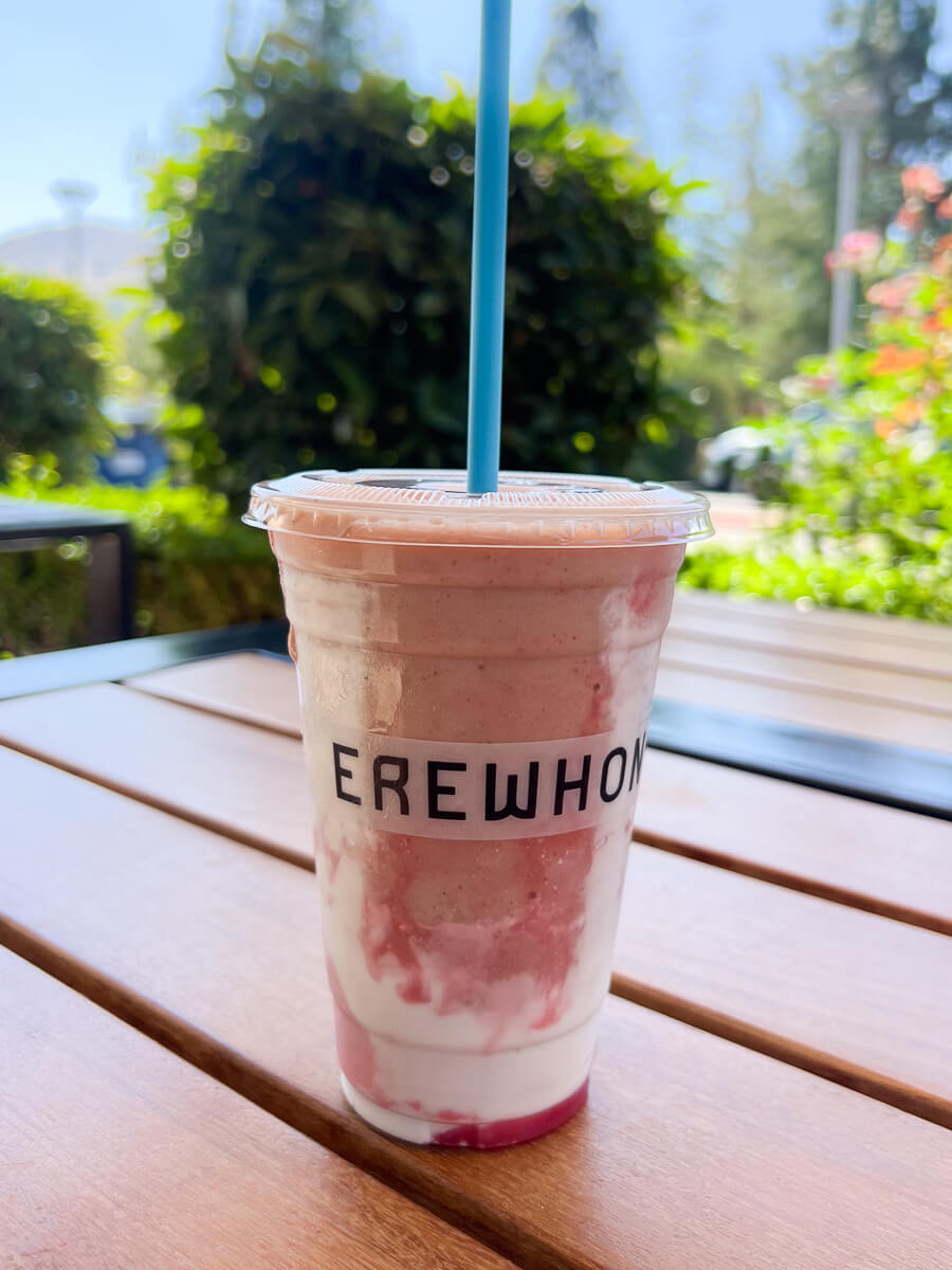 A pink Hailey Beiber Erewhon smoothie in a plastic cup that says EREWHON sits on a wood table outside at Erewhon in Calabasas, CA. 
