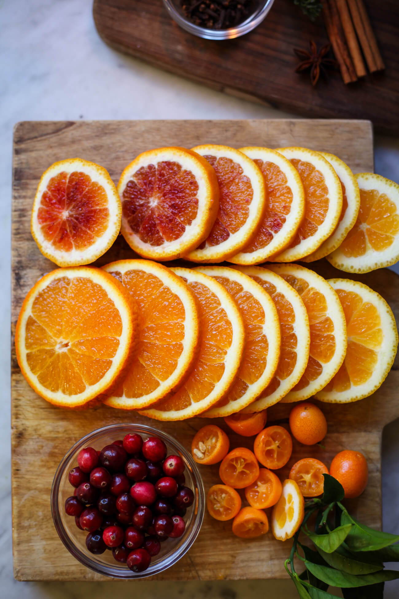 Sliced oranges and kumquats on a cutting board with a bowl of cranberries. 