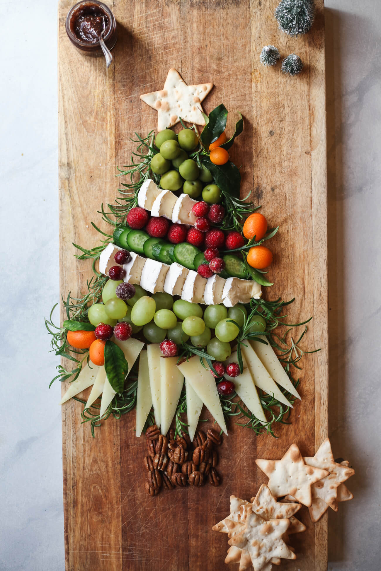Festive Christmas tree charcuterie board arranged with cheese, grapes, cucumbers, berries, kumquats, rosemary, pecans, and star-shaped crackers.