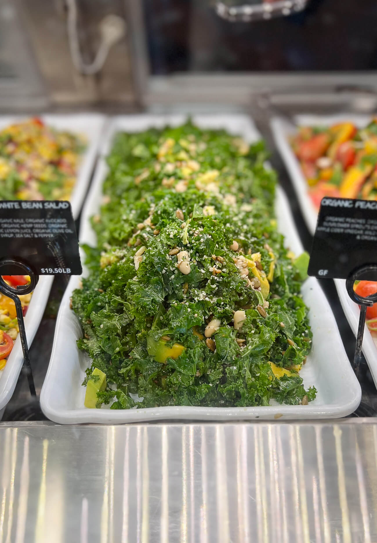 A large rectangular platter of Kale and White Bean Salad in an Erewhon deli case. 