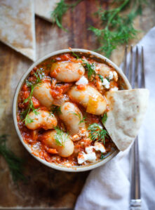 A bowl of Gigantes Plaki, a Greek recipe made with gigantes beans (giant white beans) and tomato sauce baked with feta and dill. This bowl is served with pita bread.