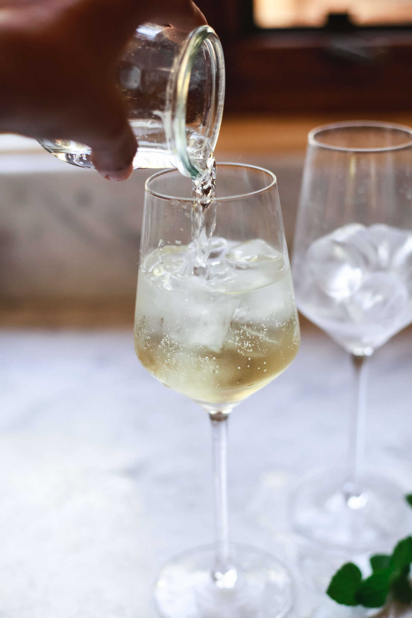 Prosecco is poured over St. Germain and ice in a wine glass to make a Hugo Spritz.