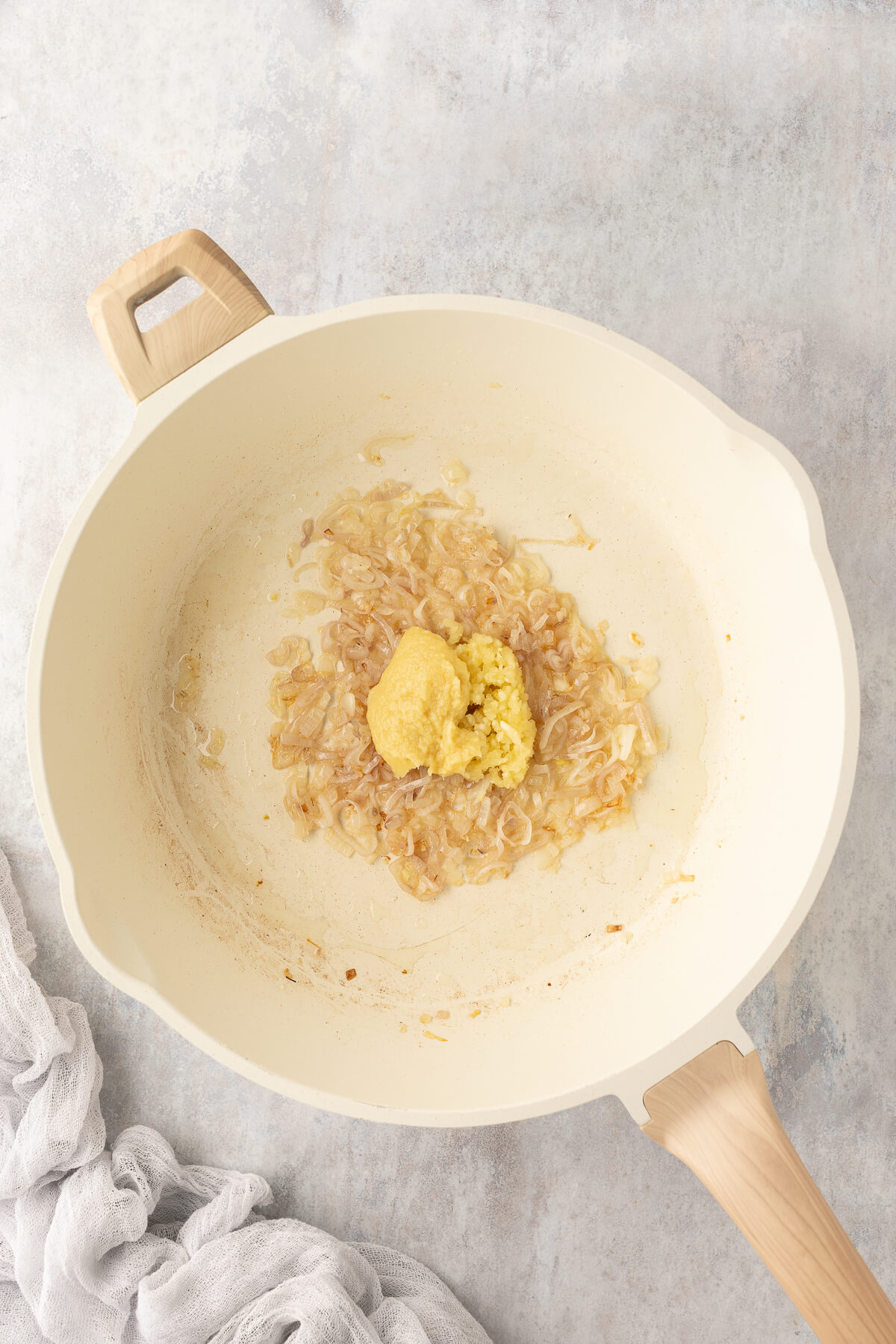 Garlic and ginger are added to cooked shallots in a ceramic pan.