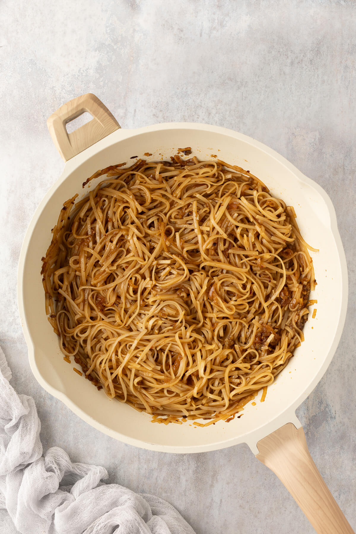 Rice noodles are coated with chili garlic sauce in a ceramic pan.