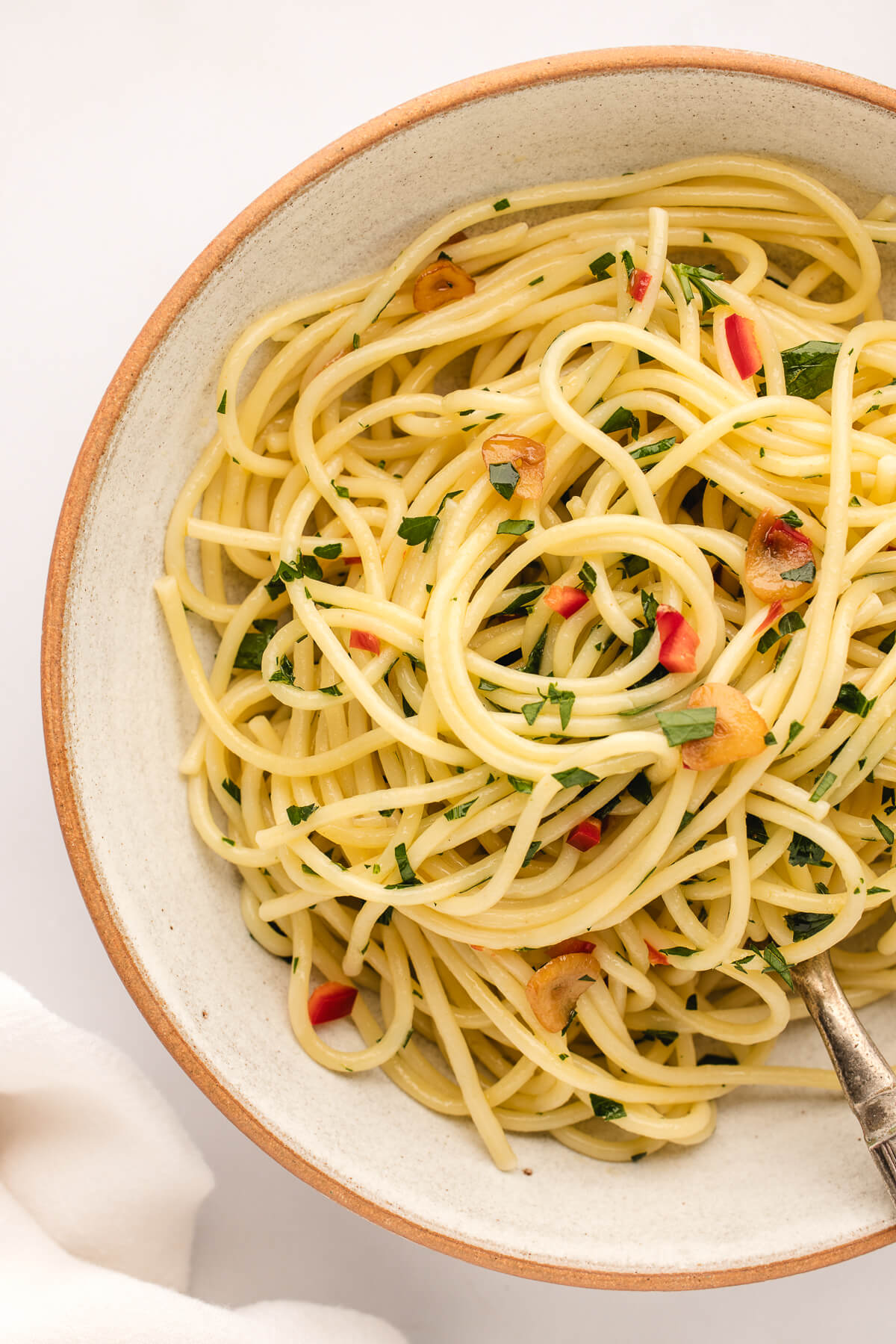 An overhead photo of a ceramic bowl filled with Spaghetti Aglio Olio e Peperoncino garnished with chopped parsley. 