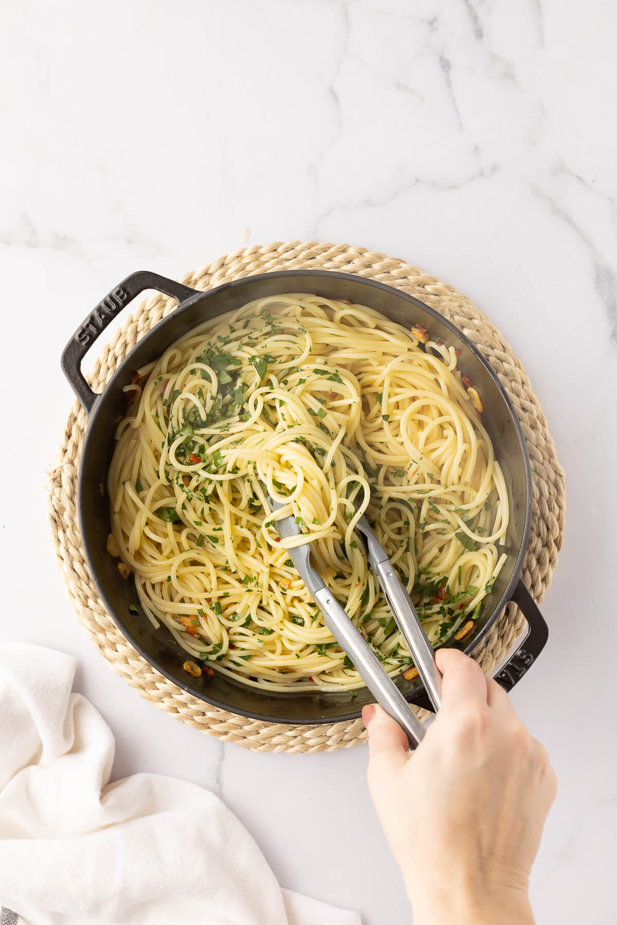 Tongs toss together cooked spaghetti with fresh parsley, olive oil, garlic, and peperoncino.