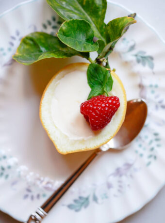 On overhead photo of a lemon posset (lemon cream) in a lemon shell. Posset is garnished with fresh mint and a raspberry.