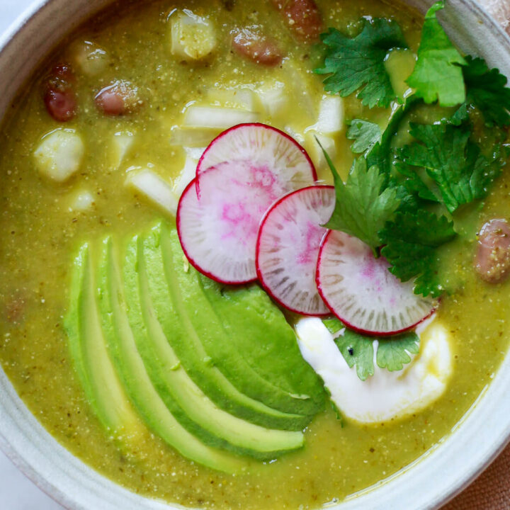 An overhead photo of a bowl of vegetarian pozole verde topped with avocado, radish, sour cream, and cilantro.