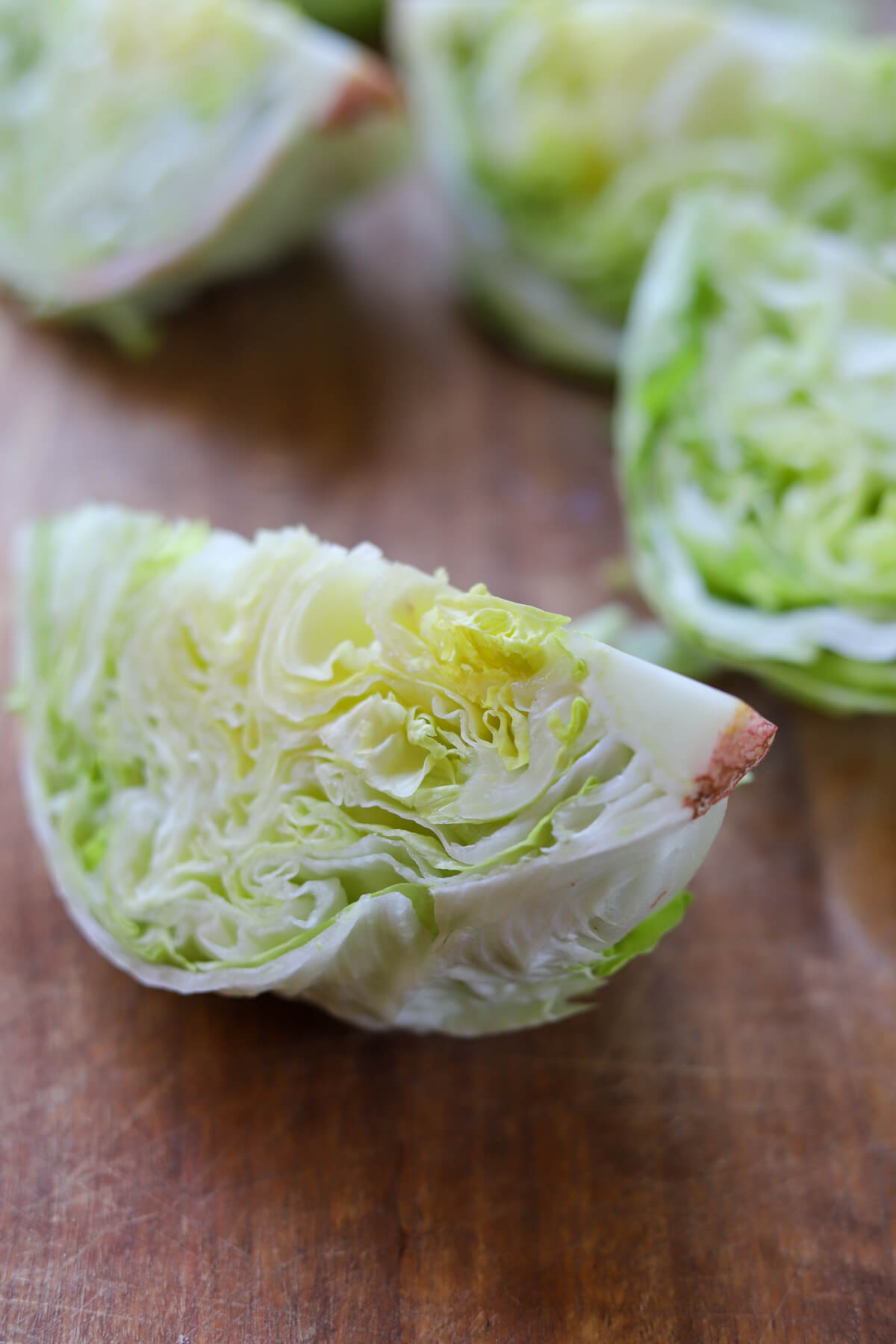 Close-up of a quartered iceberg lettuce wedge on a wooden cutting board, showing crisp green and white layers.