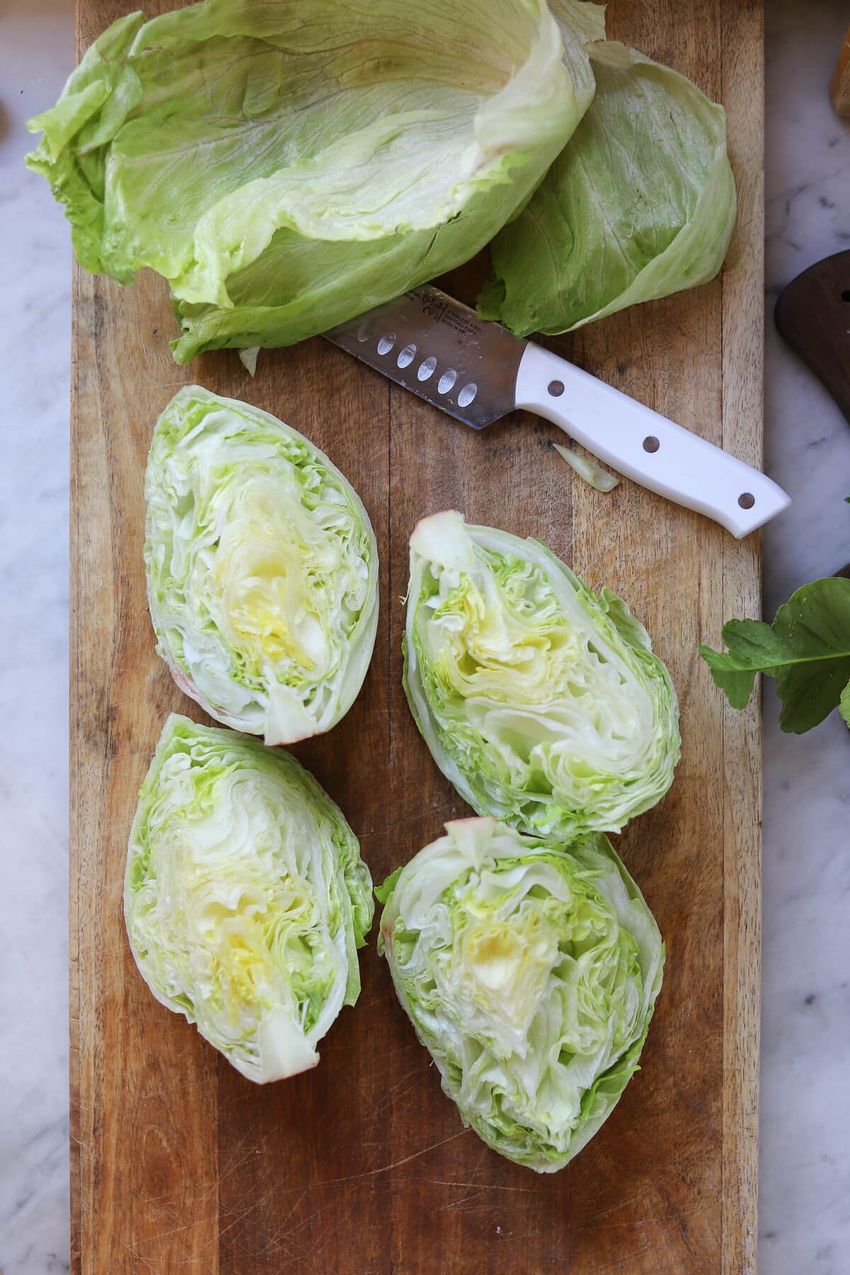 4 wedges of iceberg lettuce on a wooden cutting board with a knife to show how to cut iceberg lettuce for wedge salad.