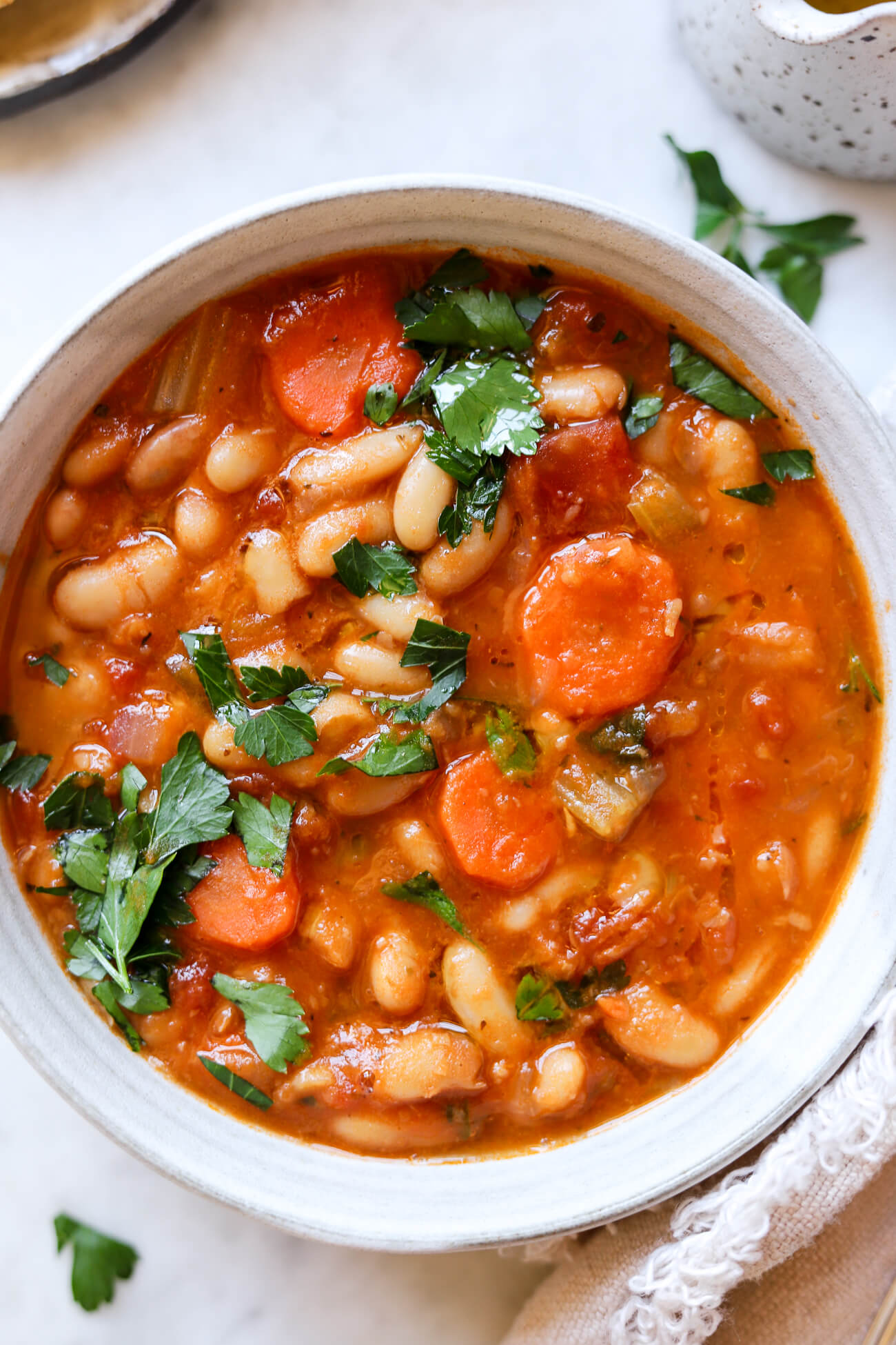 An overhead close-up photo of Greek bean soup with carrots and parsley. 
